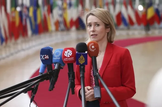 Žena u crvenom sakou govori pred grupom mikrofona.