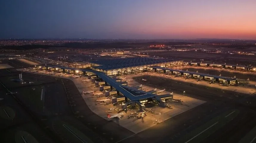 Veliki aerodrom sa avionima parkiranim na platformi tokom sumraka.