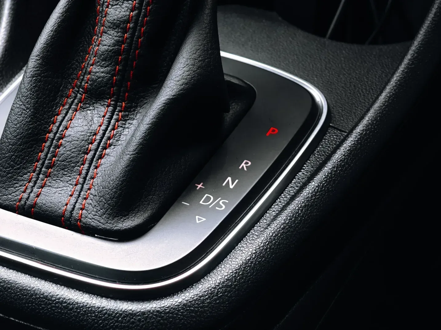 Detaljan prikaz automatskog mjenjača u automobilu, sa crvenim štepovima na kožnoj ručici i osvijetljenim oznakama stepeni prenosa (P, R, N, D/S).