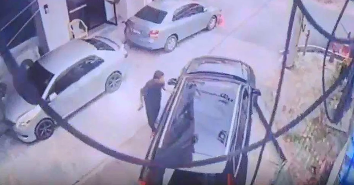 Muškarac u crnoj odjeći stoji pored srebrnog automobila na parkingu.
