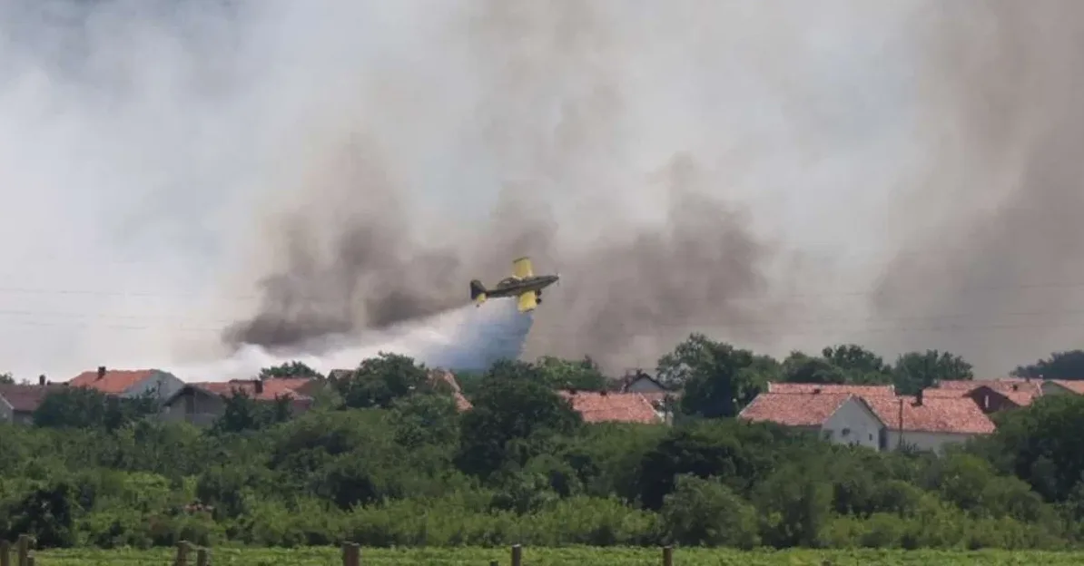 Avion za gašenje požara prska vodu iznad naseljenog mjesta okruženog dimom.