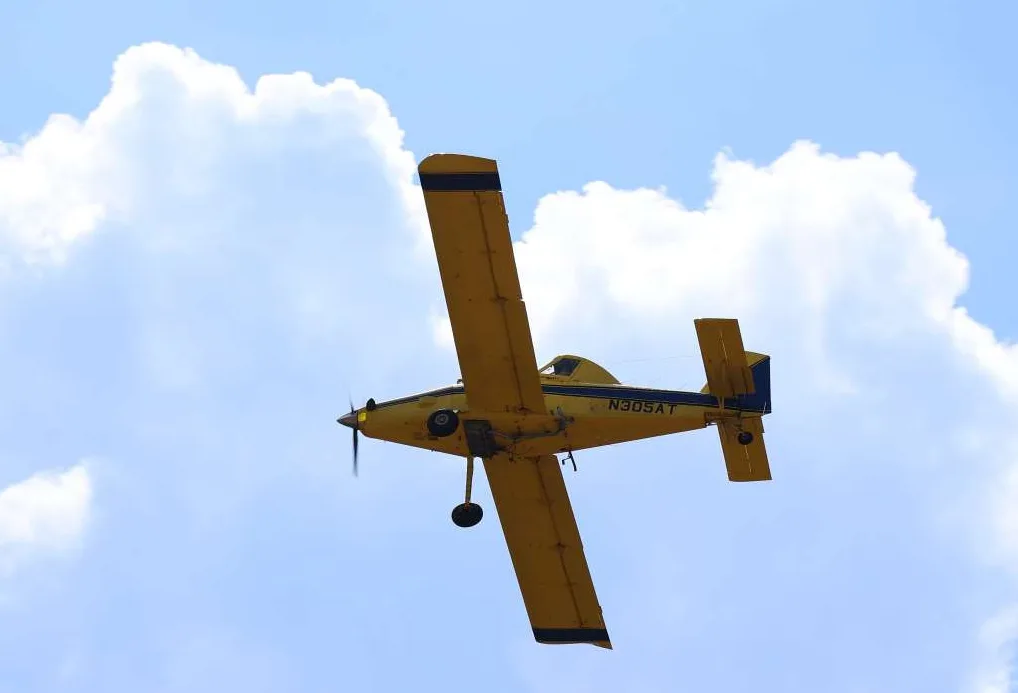 Žuti avion sa registracijskom oznakom N305AT leti na vedrom nebu sa bijelim oblacima.