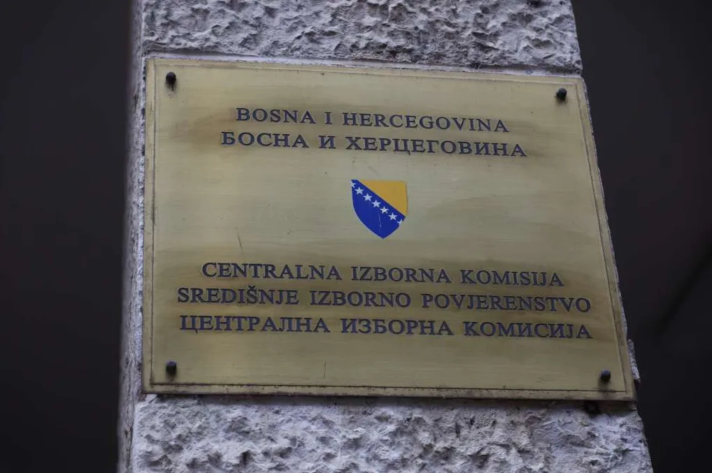 Zlatna tabla sa grbom Bosne i Hercegovine i nazivom Centralna izborna komisija na bosanskom, hrvatskom i srpskom jeziku.