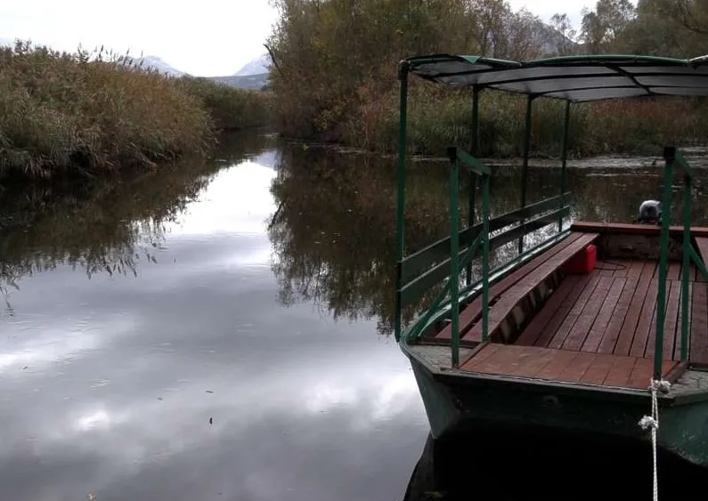 Brod sa drvenim klupama i nadstrešnicom na mirnoj rijeci okruženoj trskom i drvećem u jesenjem periodu.