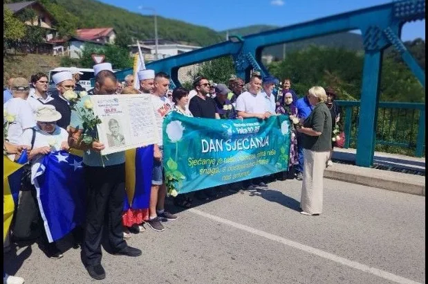 Ljudi drže zastave Bosne i Hercegovine i transparent na kojem piše "DAN SJEĆANJA" tokom komemoracije na mostu.