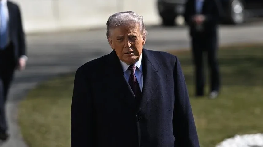 Donald Trump u tamnom kaputu i odijelu sa ljubičastom kravatom.