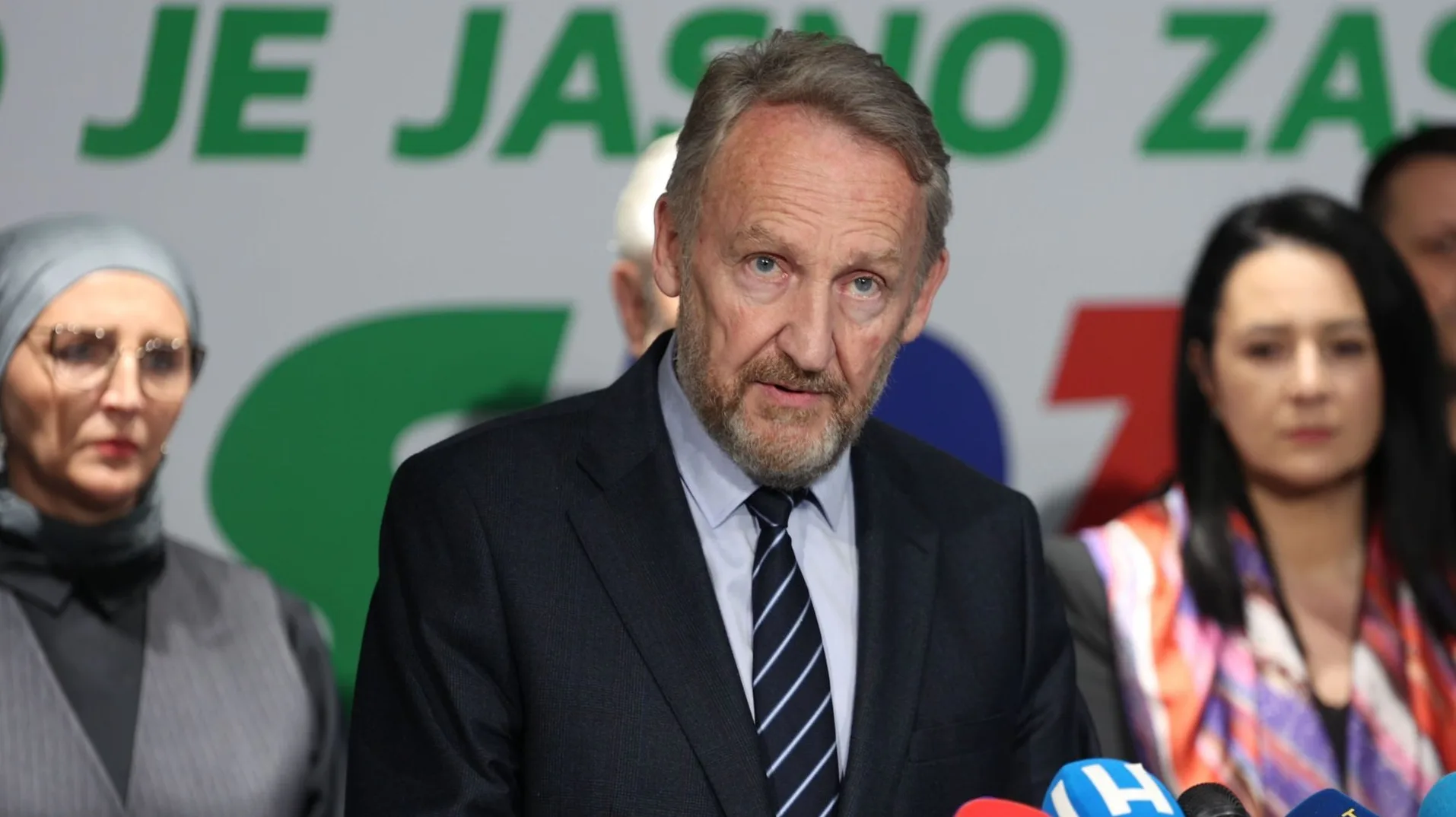 Državnik sa bradom i kravatom govori u Mostaru, okružen drugim osobama i mikrofonima.