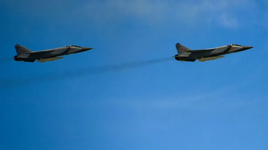Dva ruska lovca MiG-31 lete u formaciji na plavom nebu, ostavljajući tragove dima.