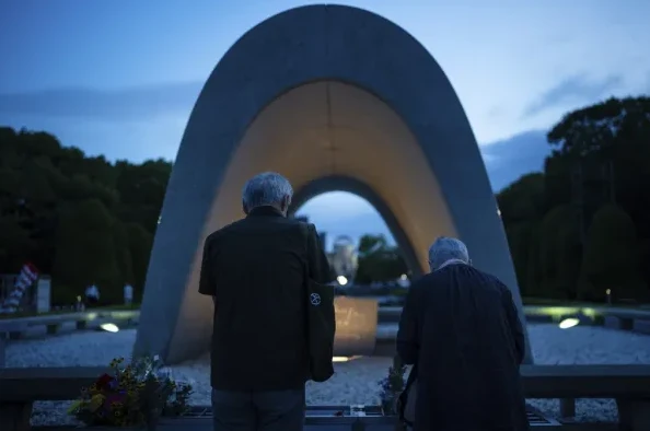 Dvoje starijih osoba stoji pred spomenikom u Spomen parku mira u Hirošimi, Japan, gledajući prema spomen-obilježju.