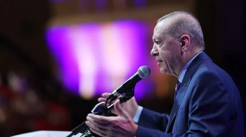 Recep Tayyip Erdoğan govori za govornicom sa mikrofonom, osvijetljen ljubičastim svjetlima.