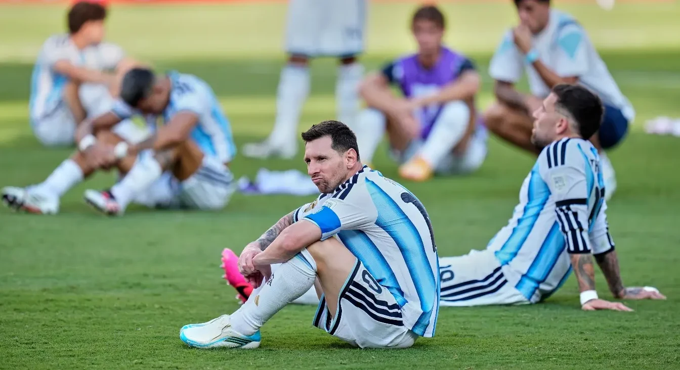 Lionel Messi i drugi fudbaleri Argentine sjede razočarani na travi nakon utakmice.