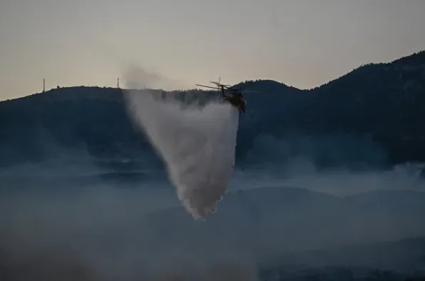 Helikopter u letu izbacuje veliku količinu vode na šumsko požarište.