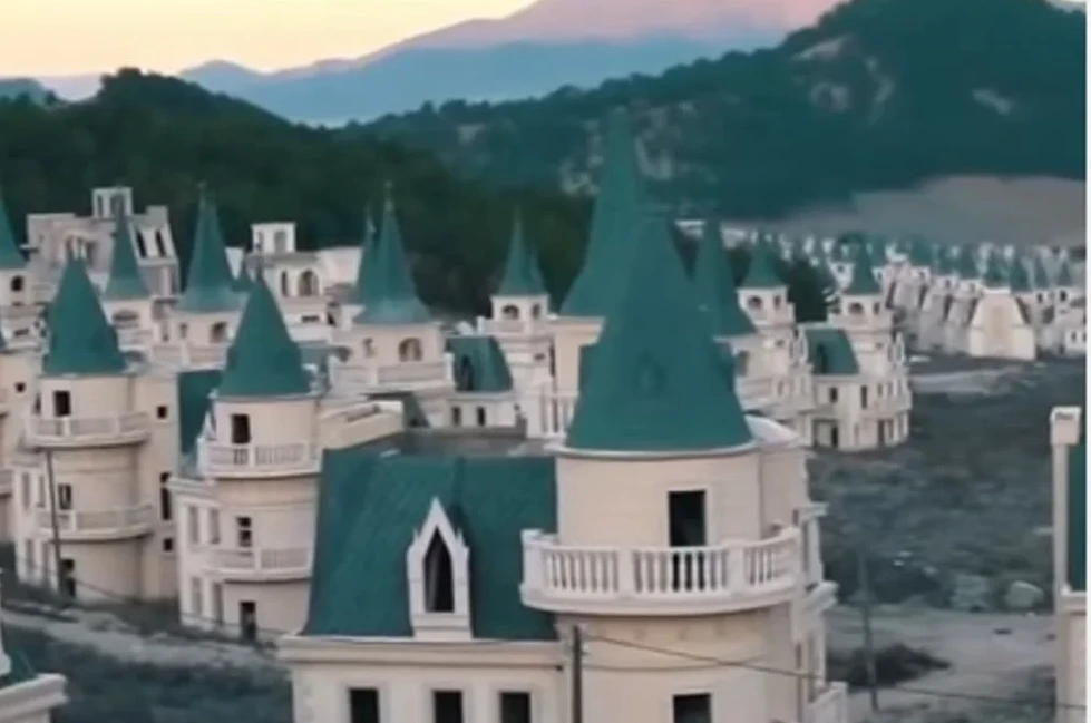 Mnoštvo modernih vila sa zelenim krovovima nalik na bajkovite dvorce, izgrađenih na obronku brda sa planinskim pejzažom u pozadini.