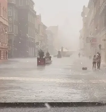 Dvoje ljudi prolazi ulicom tokom jakog pljuska.