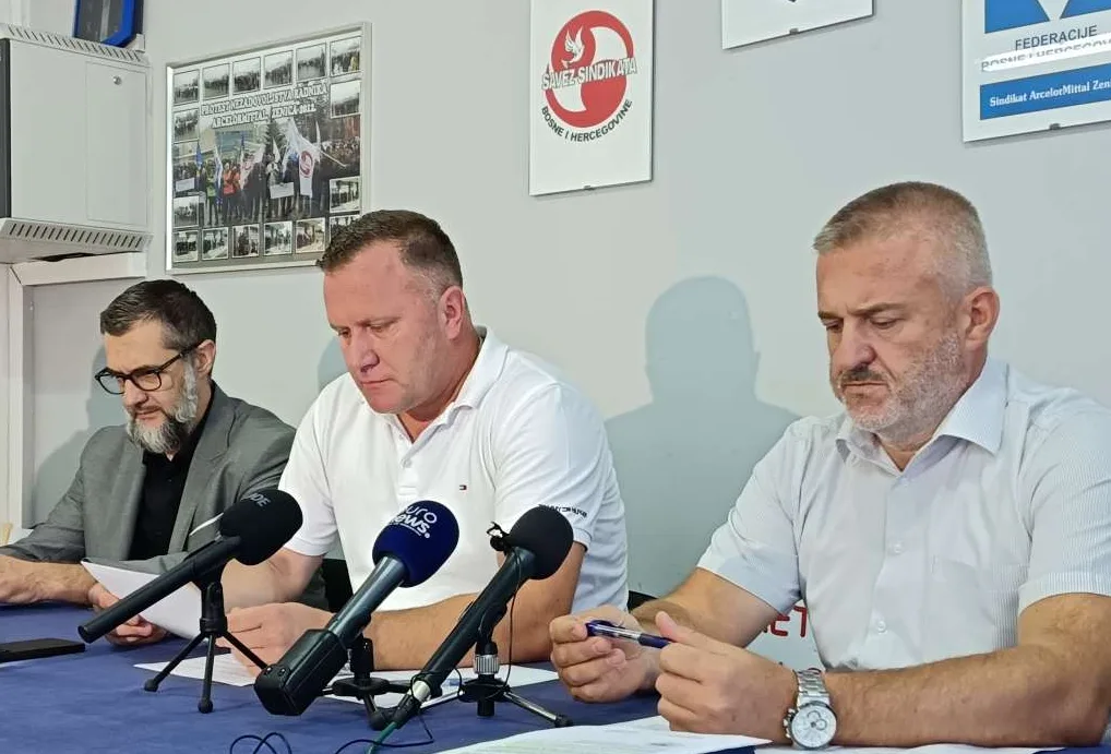 Tri muškarca sjede za stolom ispred mikrofona na konferenciji za medije.