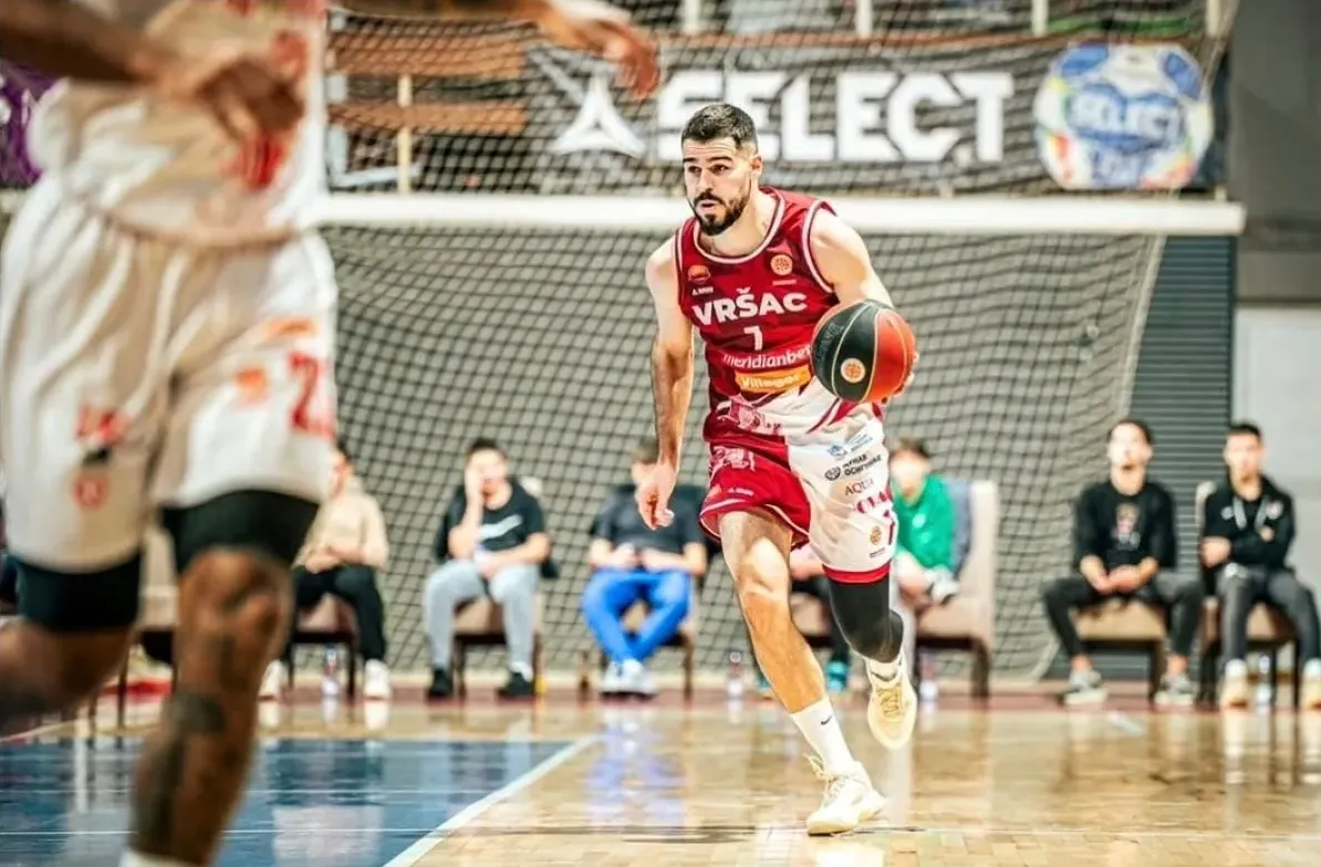 Košarkaš KK Vršac sa brojem 7 na dresu u bijelo-crvenoj opremi, u driblingu sa loptom u rukama, na parketu sportske dvorane.