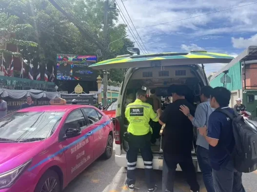 Scena na ulici sa ljubičastim taksijem i vozilom hitne pomoći, gdje se čini da medicinsko osoblje pomaže nekome da uđe u vozilo.