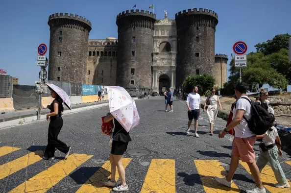 Grupa turista prelazi pješački prelaz ispred impozantnog zamka Castel Nuovo u Napulju, Italija, tokom sunčanog dana.