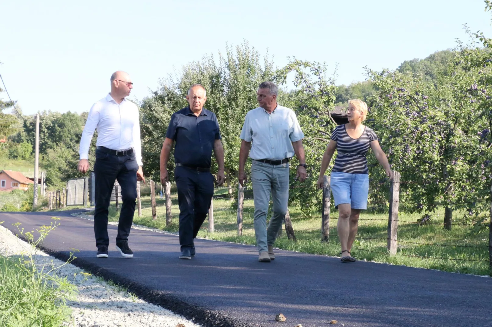 Četiri osobe, dva muškarca i dvije žene, šetaju novopoloženim asfaltiranim putem pored voćnjaka.