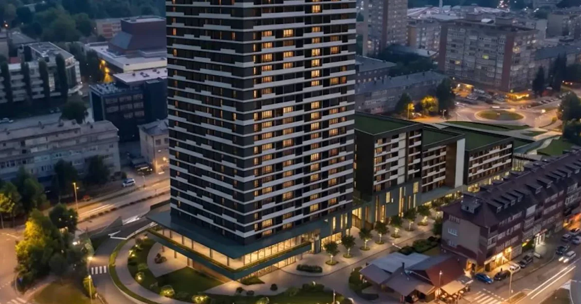 Pogled iz zraka na moderan stambeni kompleks s visokim tornjem i nižim zgradama, osvijetljen u večernjim satima.