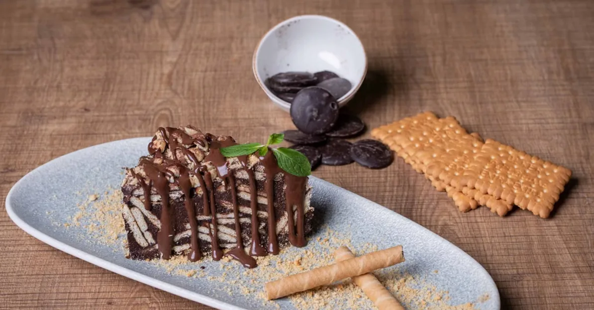 Komad čokoladne bakine torte poslužen na tanjiru, preliven čokoladnim sosom i ukrašen listićem mente.