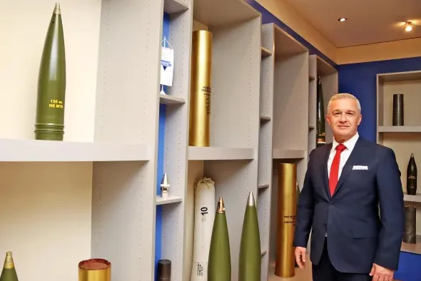 Muškarac u odijelu stoji pored izložbenih eksponata projektila.