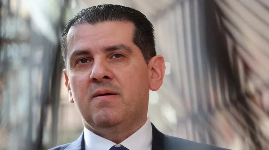 Portret muškarca u tamnom odijelu i bijeloj košulji sa plavom kravatom sa bijelim tačkicama.