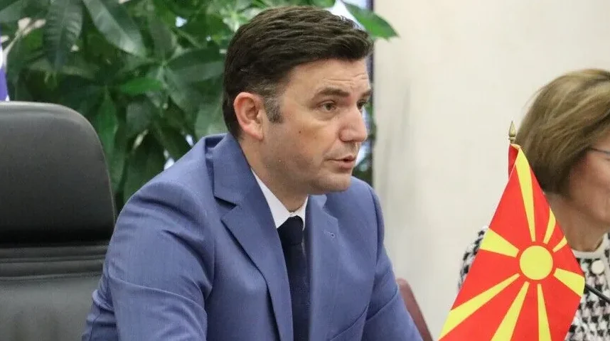 Muškarac u plavom odijelu i tamnoj kravati, gleda lijevo, pored njega se nalazi zastava Sjeverne Makedonije.