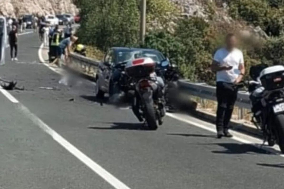 Saobraćajna nesreća sa automobilom i dva motocikla na putu, sa ljudima koji stoje okolo.