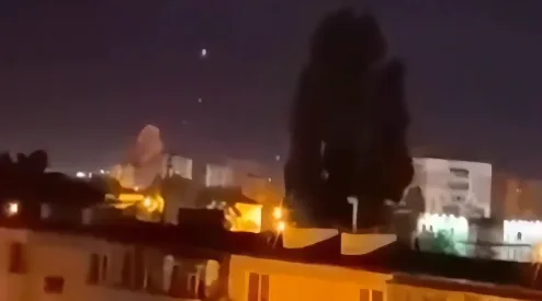 Silueta dviju osoba na vrhu zgrade u noćnom gradu, ispred njih nekoliko svjetlosnih tačaka na nebu.