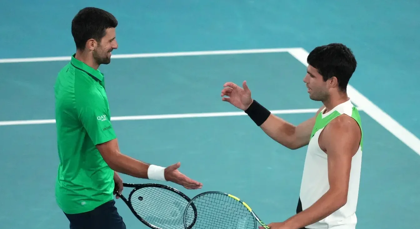 Novak Đoković i Carlos Alcaraz se rukuju nakon meča na teniskom terenu.