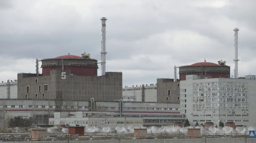 Peti blok nuklearne elektrane sa crvenim krovom i dimnjacima na oblačan dan.
