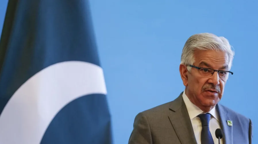 Portret Khawaje Asifa, ministra odbrane Pakistana, kako govori iza zastave Pakistana na plavoj pozadini.