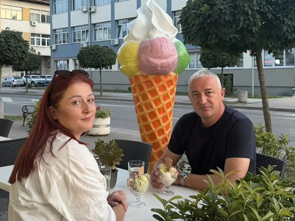 Par sjedi za stolom ispred radnje sa sladoledom, uživajući u desertu.