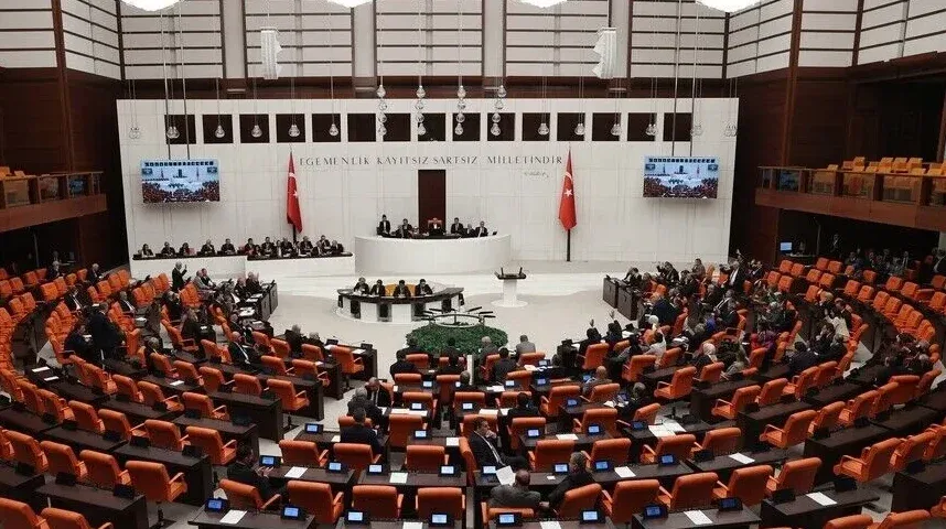 Unutrašnjost zgrade turskog parlamenta sa sjednicima koji sjede u narandžastim stolicama i zastavama Turske.