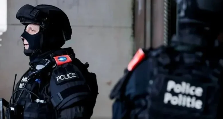 Dva policajca u punoj opremi, jedan sa kacigom i maskom za lice, a drugi sa natpisom 'Police Politie' na uniformi.