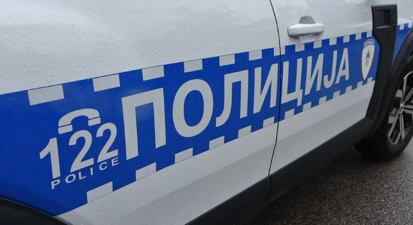 Detalj policijskog vozila sa natpisom "POLICIJA" i brojem za hitne slučajeve "122" ispisanom bijelim slovima na plavoj podlozi.