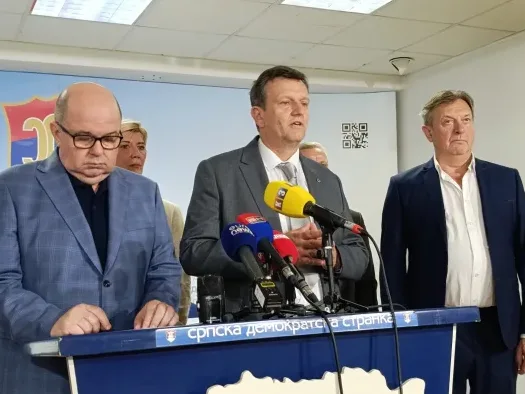 Političari ispred govornice sa mikrofonima na političkom skupu Srpske demokratske stranke.