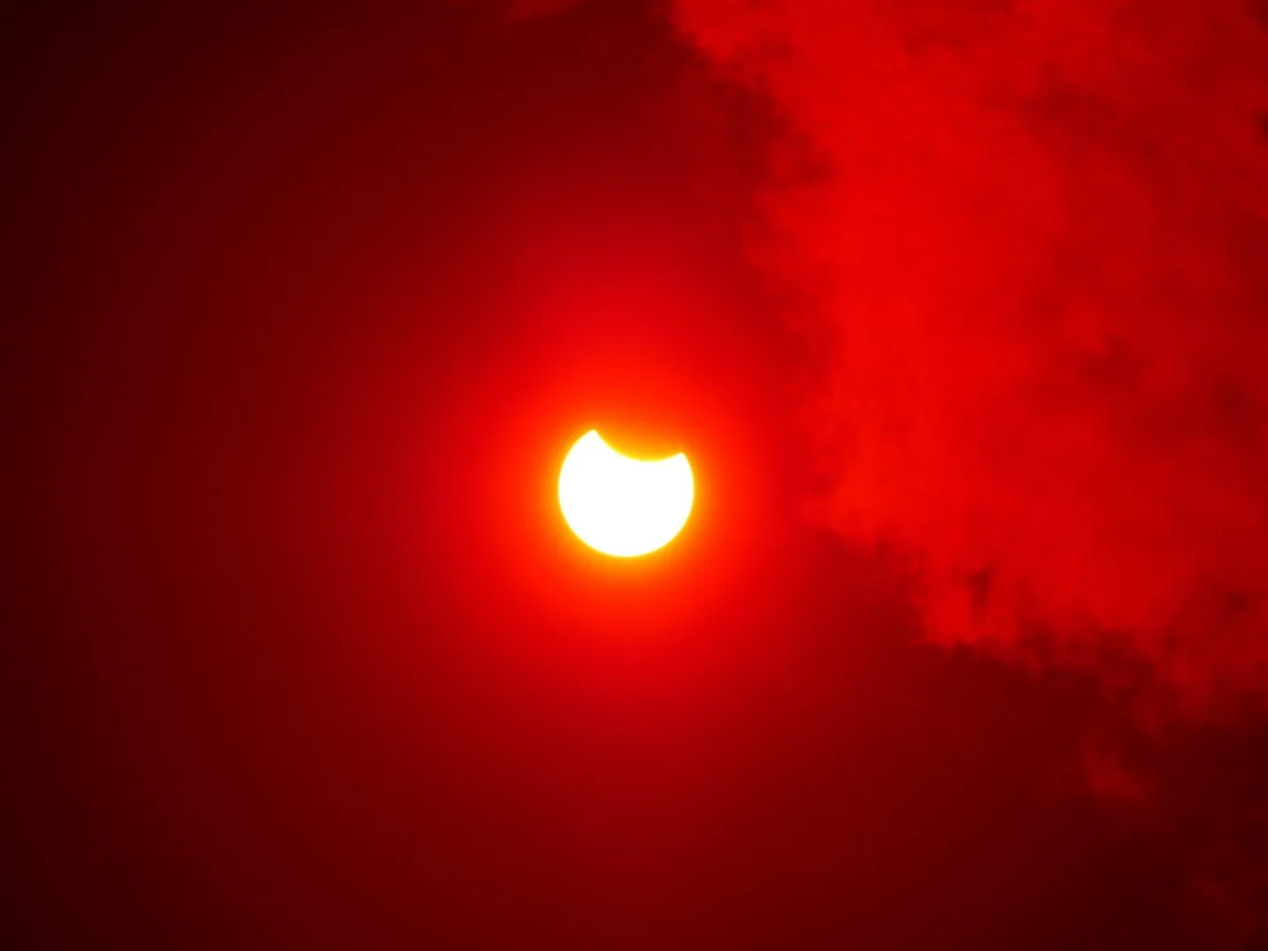 Pomračenje Sunca sa svijetlim polukrugom na lijevoj strani, okruženim crvenim oblacima.