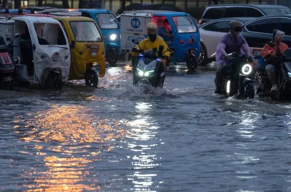 Motociklisti i vozači trikotažnih taksi vozila voze kroz poplavljenu ulicu