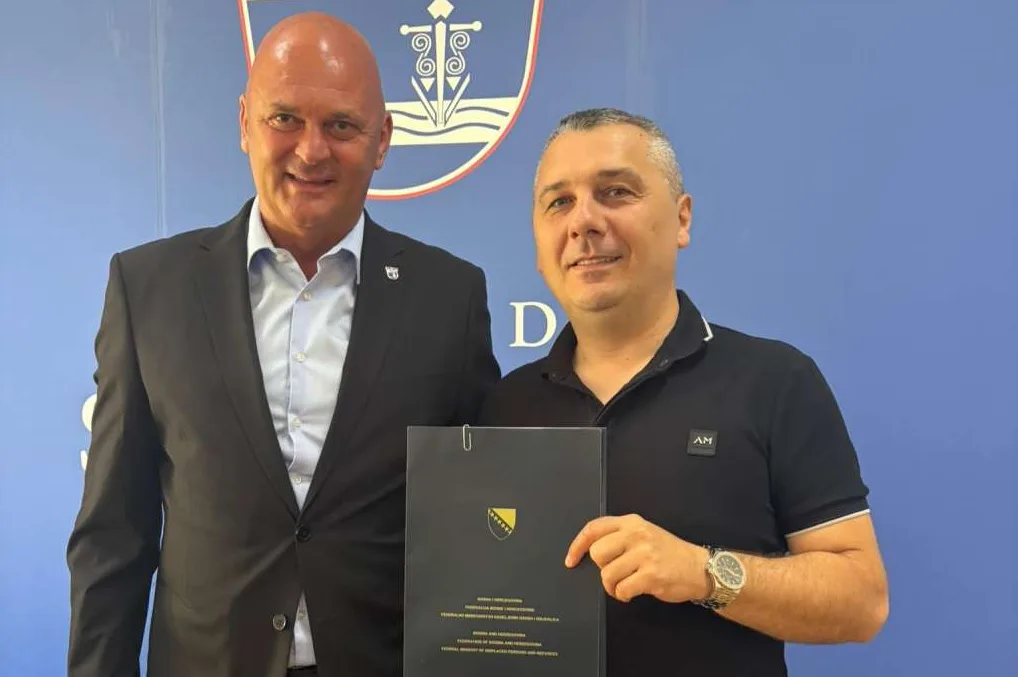 Dva muškarca poziraju sa dokumentom ispred plave pozadine sa grbom FBiH.