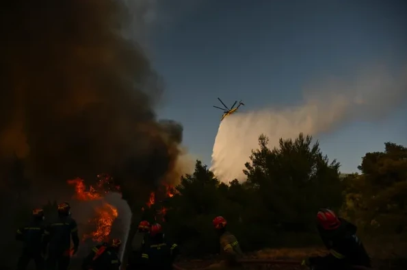 Helikopter baca vodu na šumski požar dok vatrogasci gase vatru s tla.
