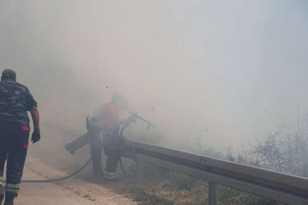 Vatrogasci se bore sa požarom okruženi gustim dimom, jedan koristi crijevo.