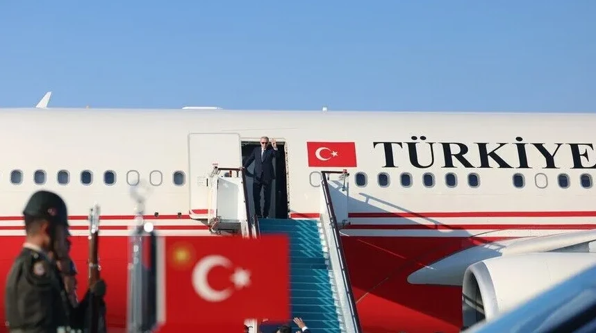Predsjednik Turske, Recep Tayyip Erdoğan, silazi niz stepenice aviona sa logom Turske na repu, dok ga dočekuje počasna garda i turska zastava.