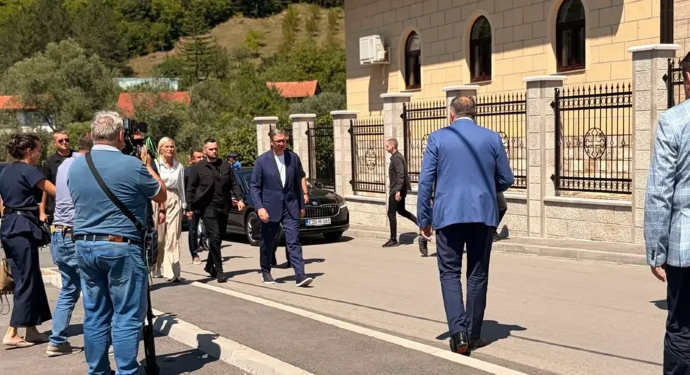 Predsjednik Srbije Aleksandar Vučić u plavom odijelu hoda ulicom u pratnji obezbjeđenja i novinara.