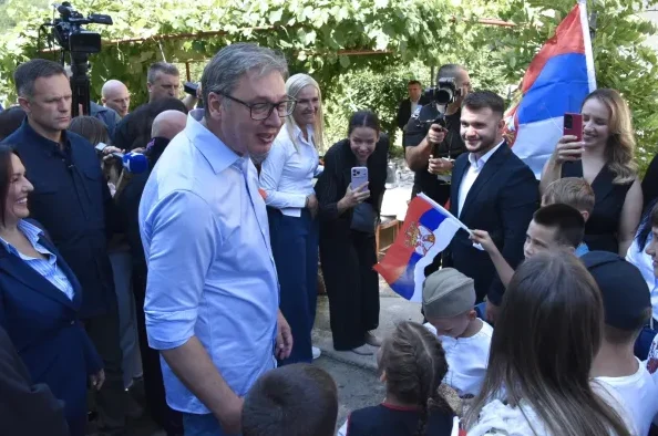Predsjednik Srbije Aleksandar Vučić razgovara sa građanima, u pozadini se vide zastave Srbije i ljudi sa mobilnim telefonima.