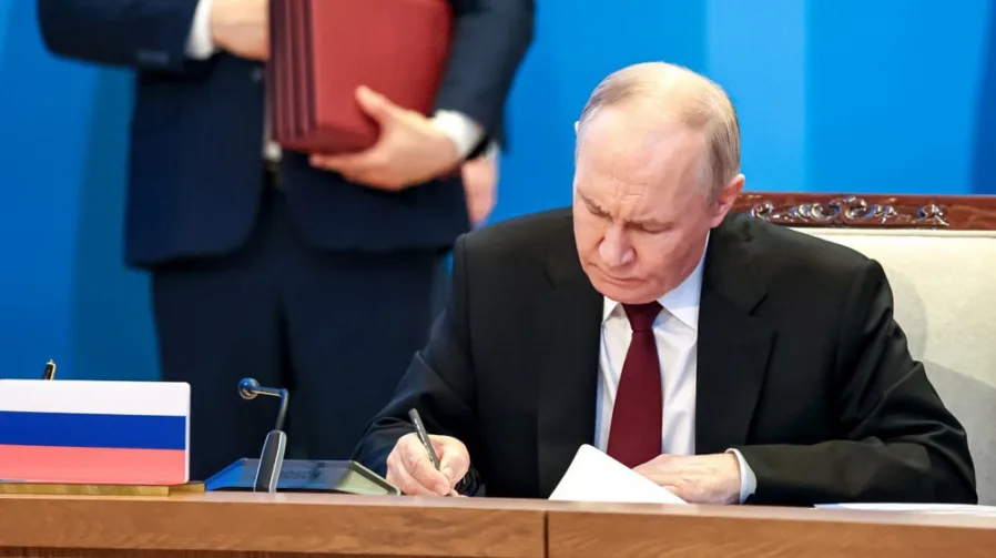 Vladimir Putin potpisuje dokument, pored ruske zastave