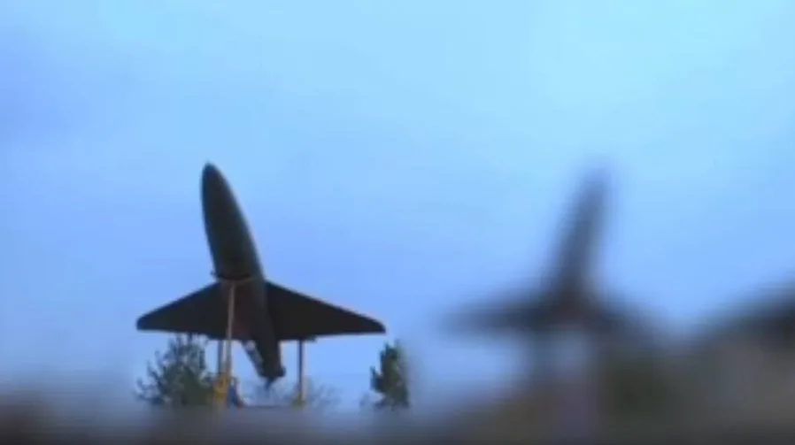 Raketa na postolju na otvorenom prostoru, sa drugim zamućenim objektima u pozadini.