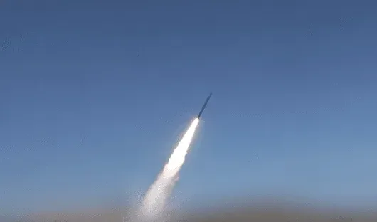 Raketa lansirana u vedro plavo nebo sa gustim bijelim dimom koji izbija iz njenog repa.