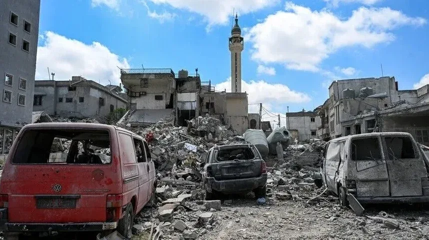 Uništeni grad sa minaretom i zapaljenim vozilima na hrpi ruševina.